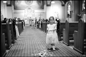 A flower girl in white dress scatters petals down the aisle of a traditional church wedding.