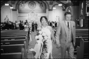Black and white photo of bride and groom walking down church aisle after wedding ceremony.