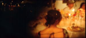 Candlelit dinner scene with a woman in a strapless dress seen from behind at a warmly lit table.