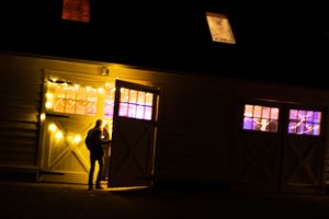 A silhouetted figure stands in the glowing doorway of a barn venue at night.