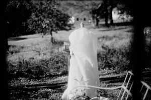 Black and white photo of a bride in a flowing veil standing outdoors among trees.
