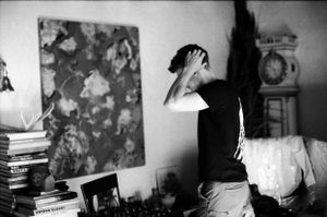 Black and white photo of a person running hands through hair in a room with artwork and books.