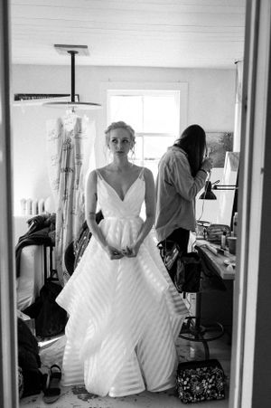 Bride in a white striped ball gown stands in a mirror reflection during wedding preparations.