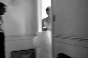 Blurry black and white photo of a bride in white dress moving through an interior hallway.