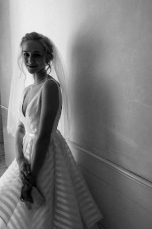 Elegant bride in a striped ball gown and veil poses against a wall in black and white photo.