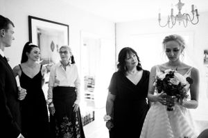 Bride holding a dark bouquet walks with family members during wedding preparations in black and white.