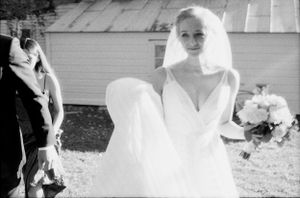 Radiant bride in a flowing white gown holding a bouquet outdoors in a black and white photo.