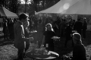 Black and white photo of guests mingling outdoors near a white tent at an event.