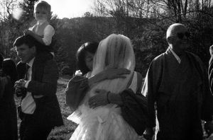 Black and white photo of a bride in veil embracing a guest outdoors at a wedding.