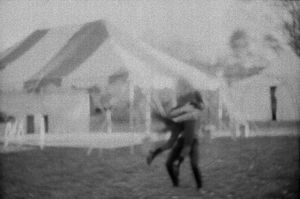 Grainy black and white photo of people dancing outside a white tent at a wedding.