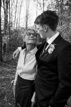 Black and white photo of an older woman and a young groom embracing outdoors.