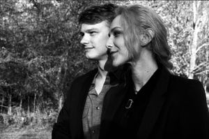 Black and white portrait of a young man and older woman standing together outdoors among trees.