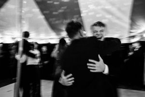Black and white blurry photo of two men hugging at a wedding reception.