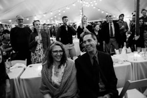 Guests laugh and celebrate at a wedding reception under a white tent with string lights.