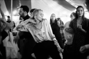 Black and white photo of a woman dancing joyfully at an indoor event.