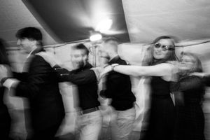 Blurred black and white photo of guests dancing energetically at a wedding reception under a tent.