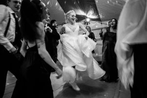 Black and white wedding reception photo of a joyful bride in a white gown dancing with guests.