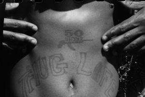Black and white photo of a person's torso with 50 Cent and Thug Life tattoos.