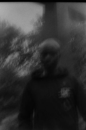 Dark moody black and white blurred portrait of a person standing outdoors among trees.