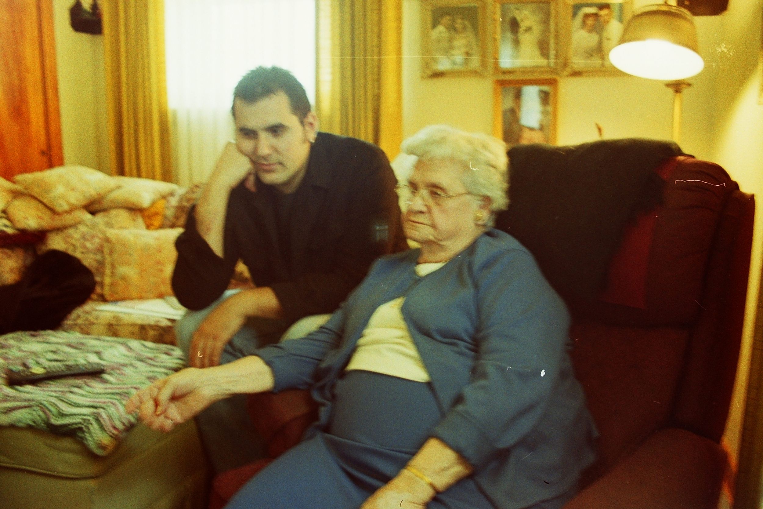 Elderly woman and younger man sitting together on a red sofa at home.
