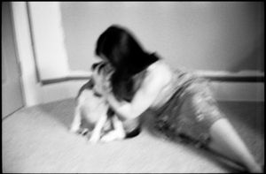 Blurry black and white photo of a woman playing with a small dog on the floor.