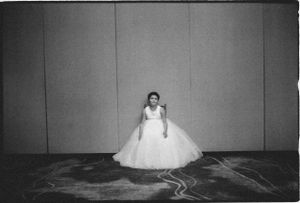 Bride in a full white ball gown standing alone in a large empty room.