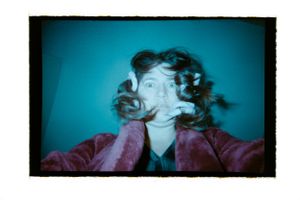 A person with wild curly hair making a funny face in a colorful photo.