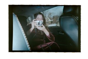 A young woman photographs with a film camera while sitting in the backseat of a car.