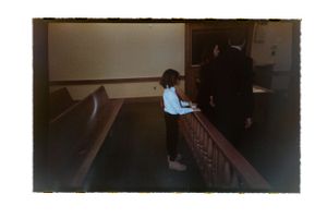 A young child stands at a wooden pew beside an adult in a church.