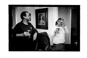 Two people holding drinks and laughing in a room with a portrait on the wall.