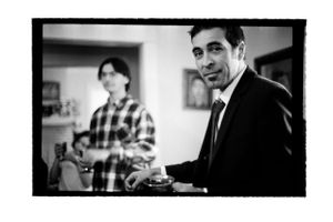 Black and white portrait of two men in a home, one in a suit facing the camera.