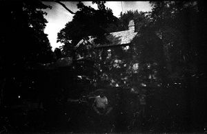 Dark black and white photo of a house surrounded by trees at night.