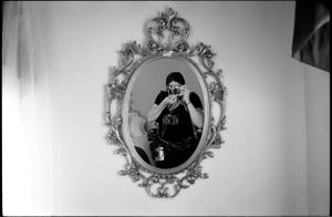 Black and white self-portrait of a photographer reflected in an ornate oval decorative wall mirror.