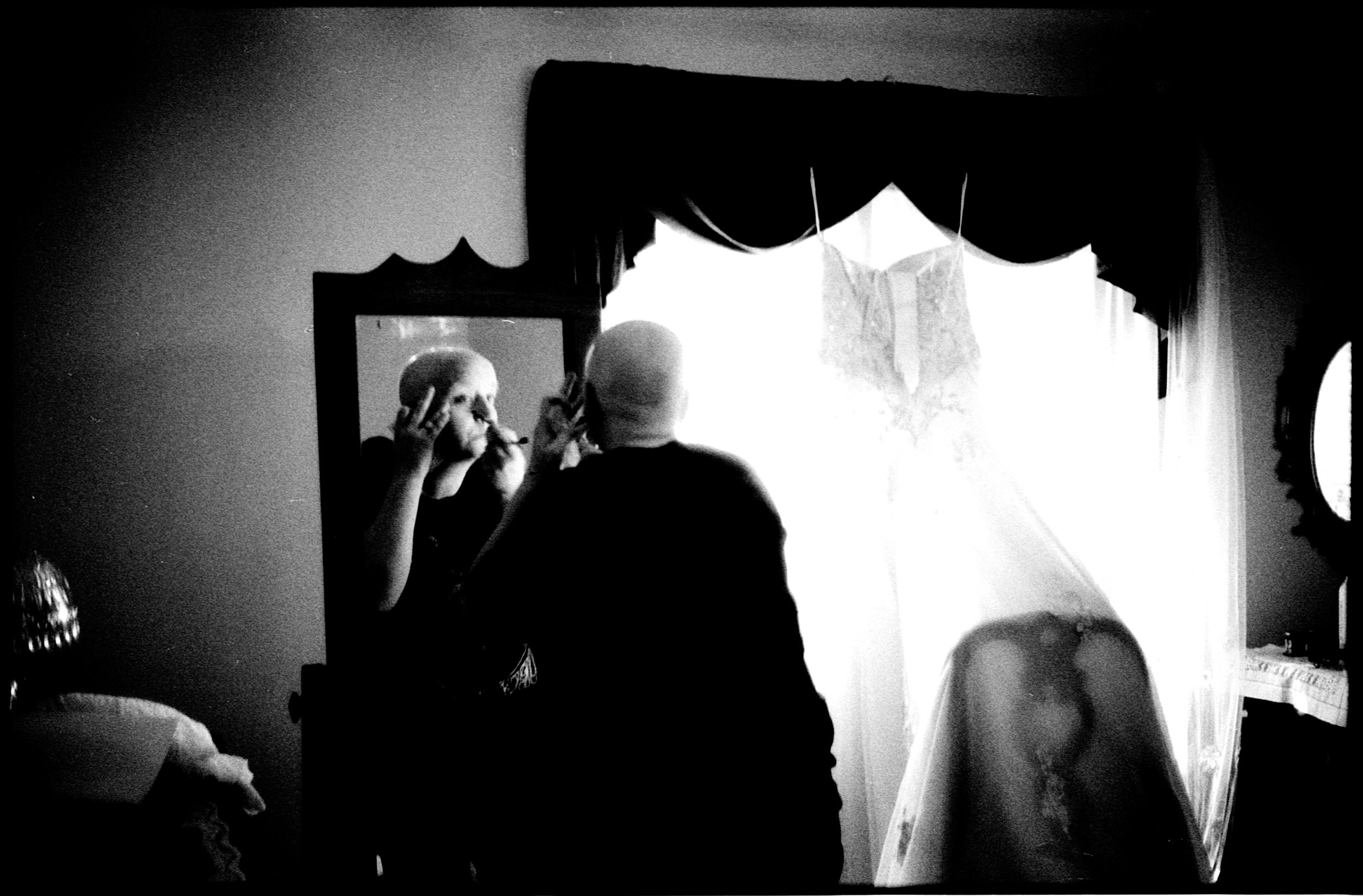 Black and white photo of people near a mirror in a dark draped room.