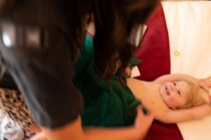 Woman in green dress tending to a smiling baby lying on a red surface.