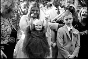 Bridesmaid holding a toddler flower girl while a young boy in a suit stands nearby.