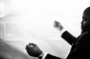 Black and white photo of a man in a suit checking his watch at a wedding ceremony.