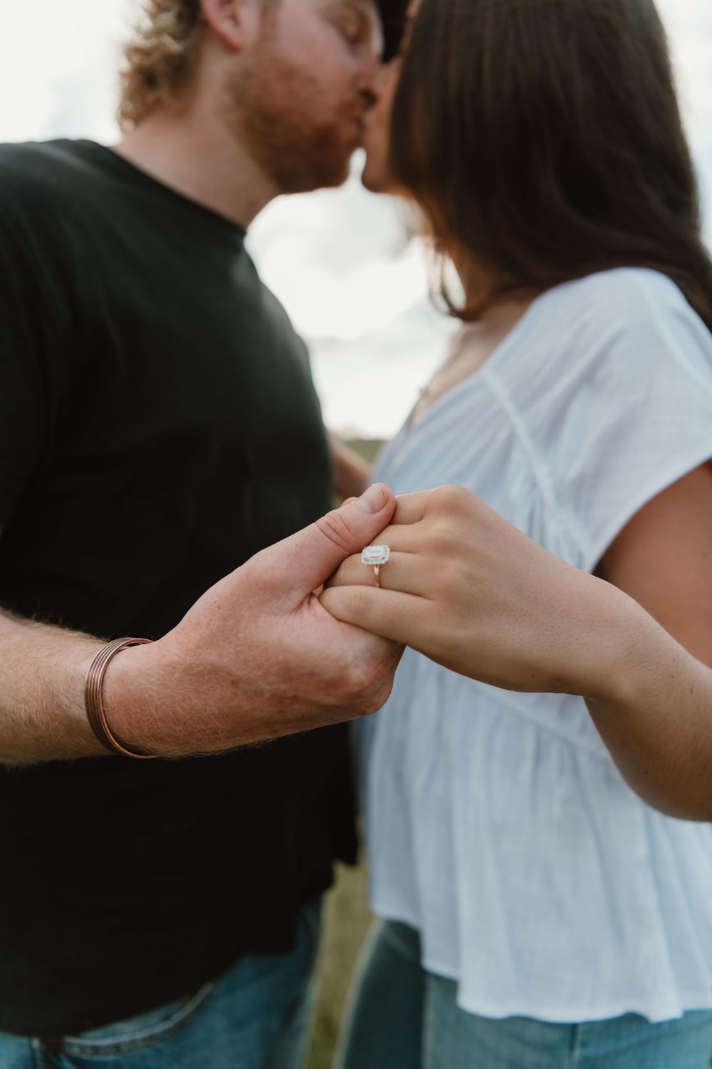 Couple sharing a kiss while showing off an engagement ring, symbolizing a romantic proposal moment.