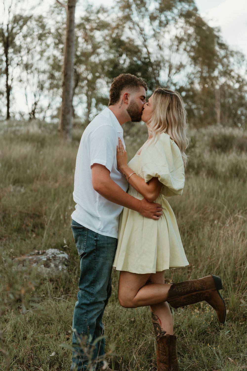 A romantic couple embraces on a rustic wooden fence in a golden meadow during sunset. in Boonah Queensland