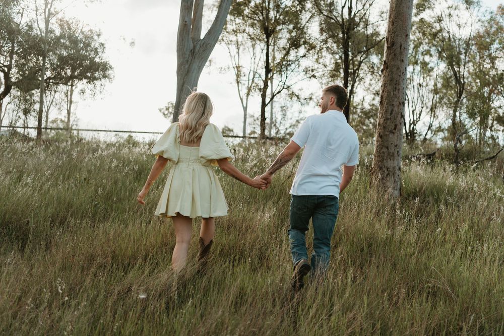 A couple walks hand in hand through a grassy field surrounded by tall eucalyptus trees at sunset. in Boonah Queensland
