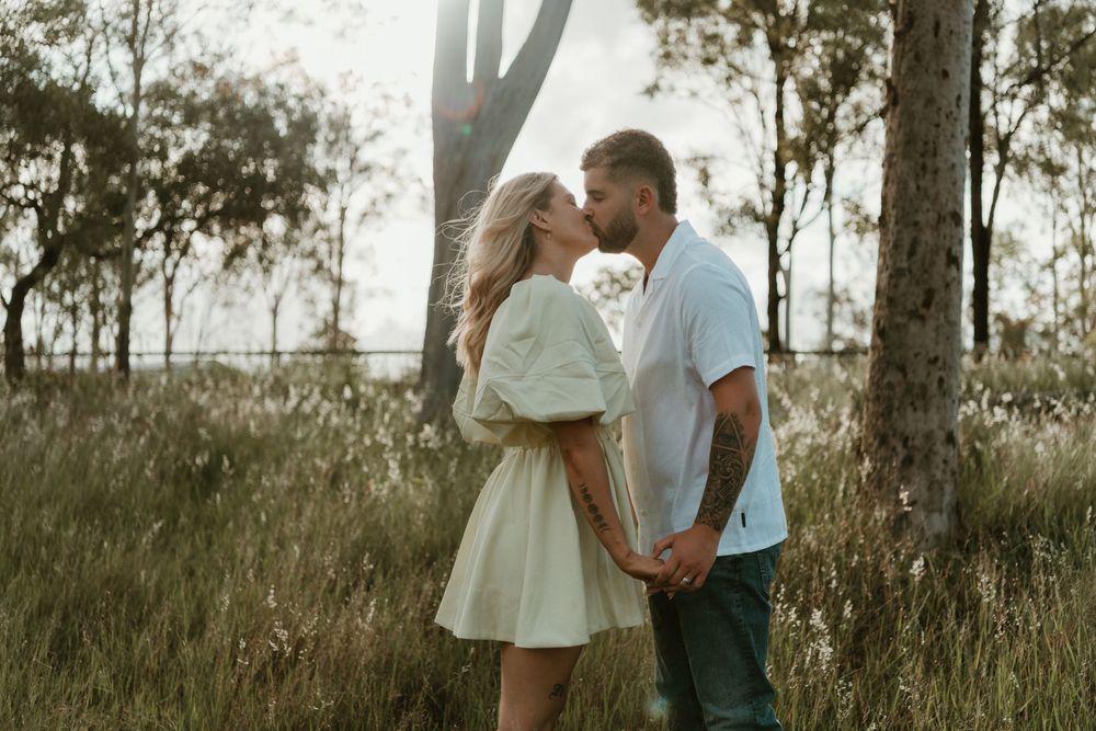 Romantic couple embraces in a sunlit meadow with tall grass and trees during golden hour sunset. in Boonah Queensland