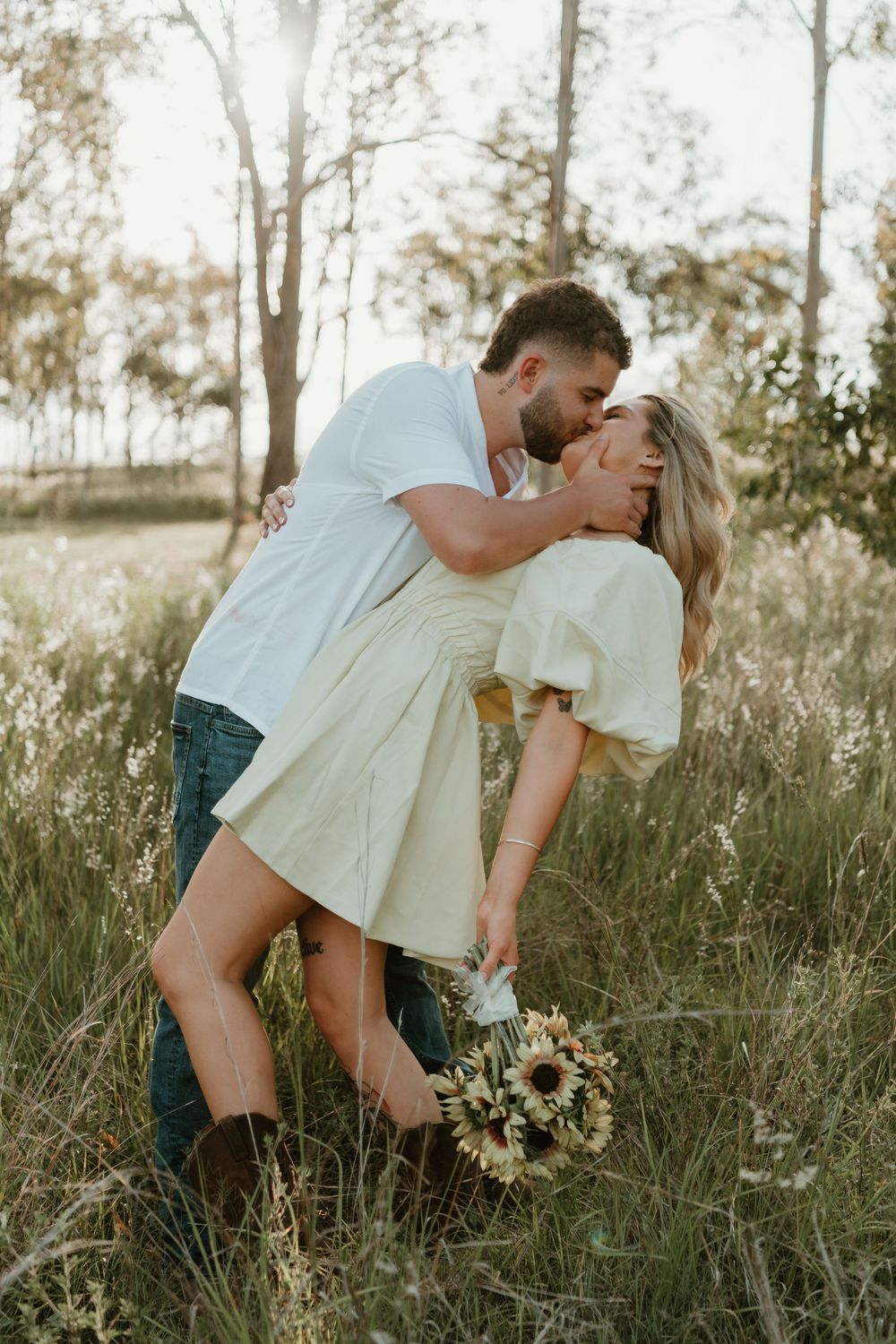 A romantic couple shares a tender kiss while standing in a sunlit field of tall grass during golden hour. in Boonah Queensland