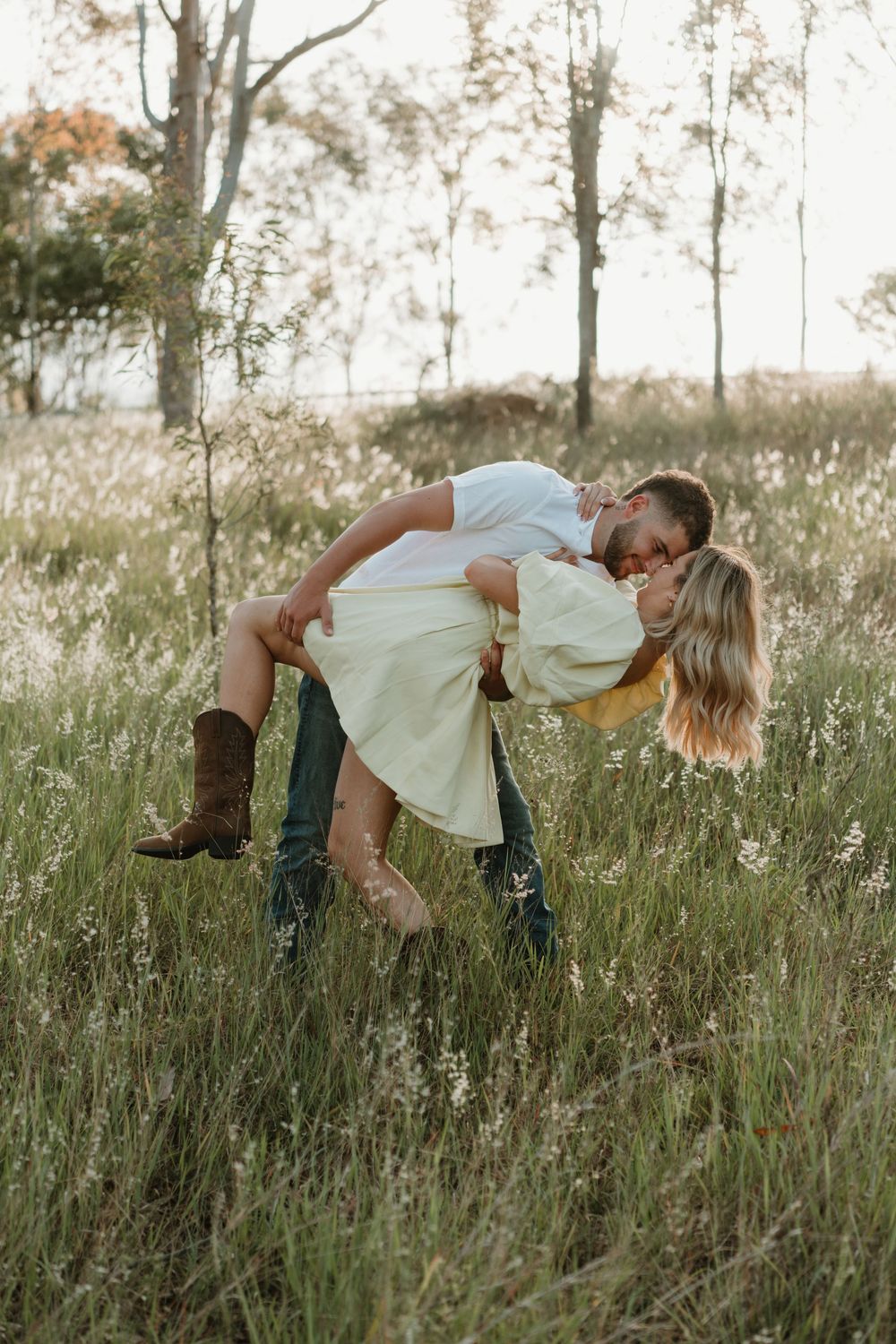 A couple embraces in a romantic dip pose while standing in a tall grass field at sunset. in Boonah Queensland