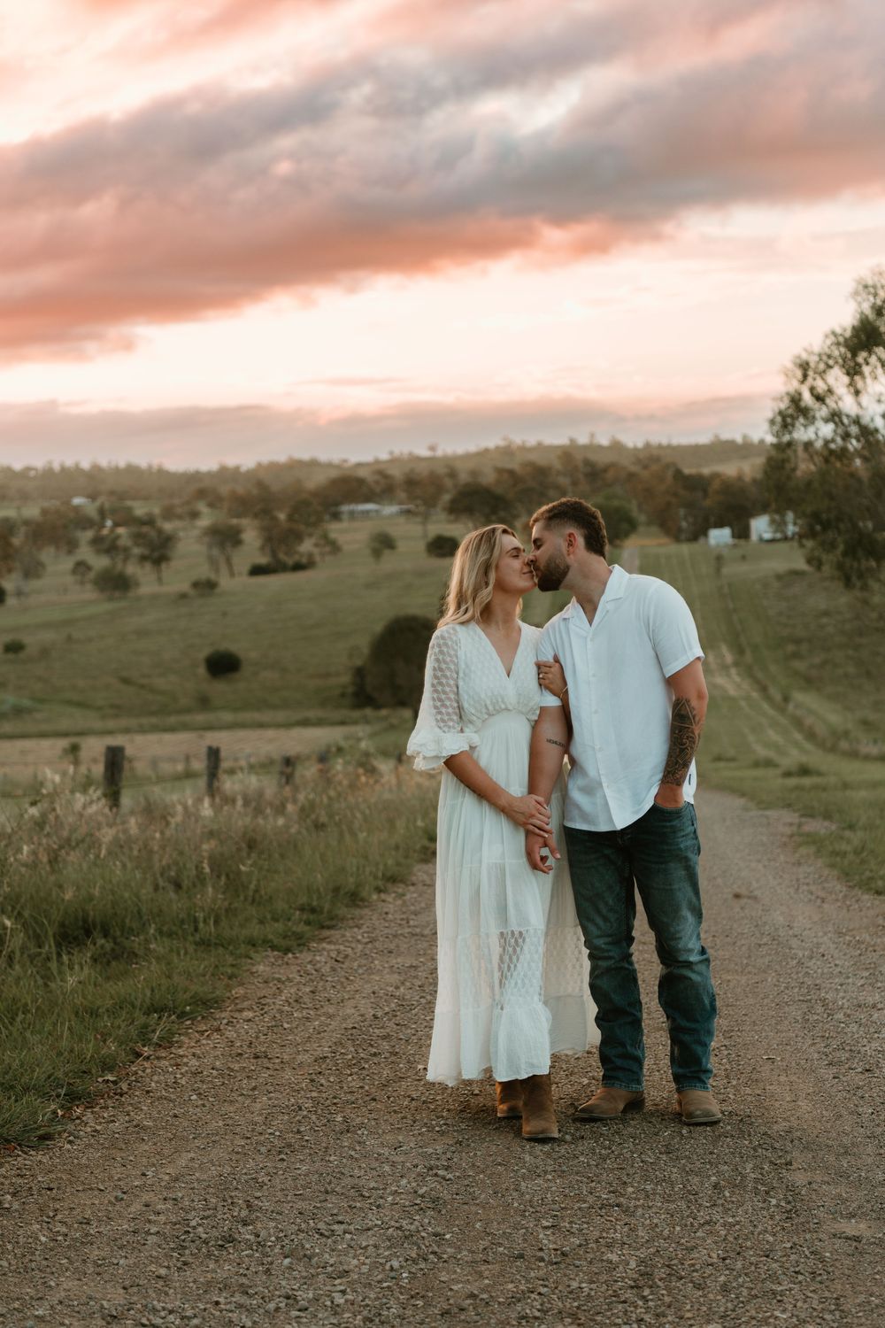 A couple in white and denim share an intimate moment on a rural dirt road at sunset. in Boonah Queensland