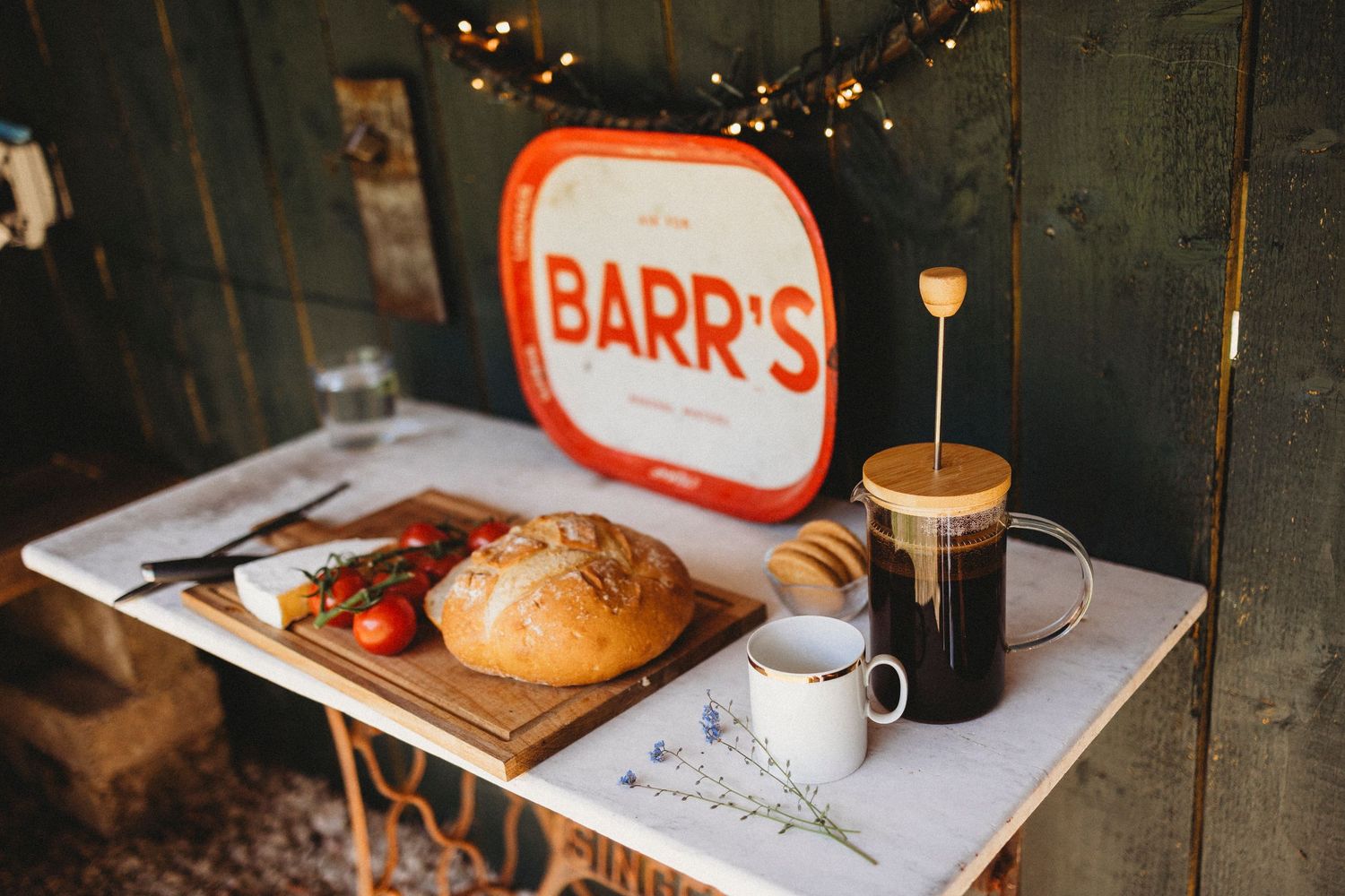 A rustic breakfast setup with sandwich, tomatoes, coffee and an orange Barr's vintage sign on a white tray. Google my bussines photography
