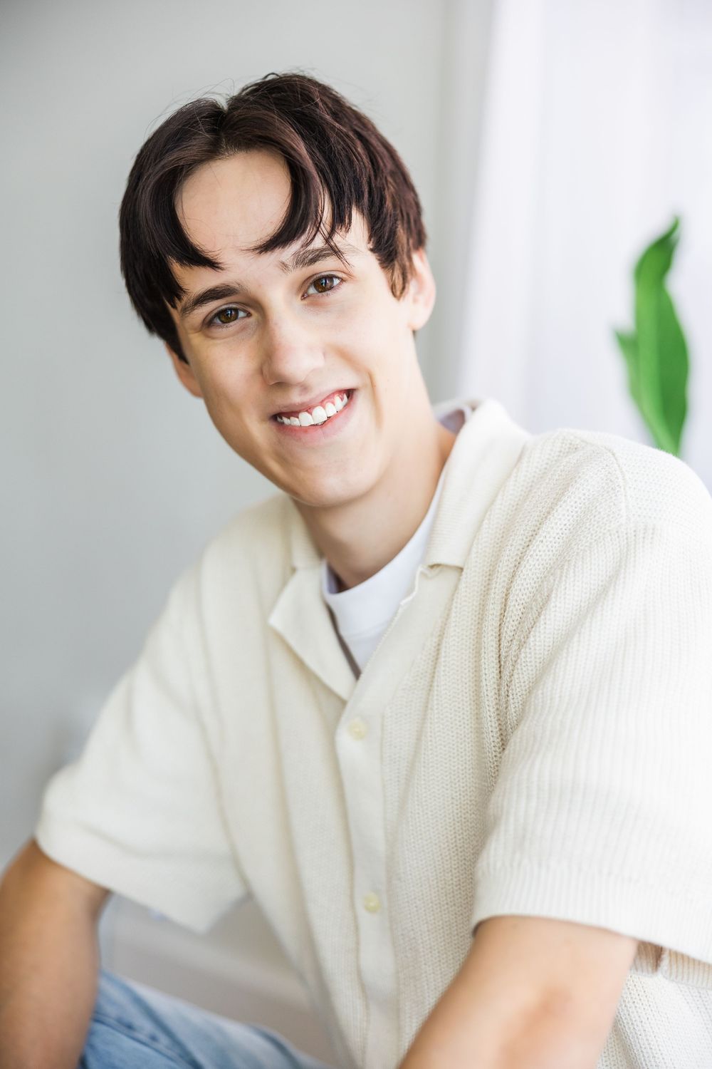 Smiling young man with dark hair wearing a cream ribbed button-up shirt in a bright indoor setting.