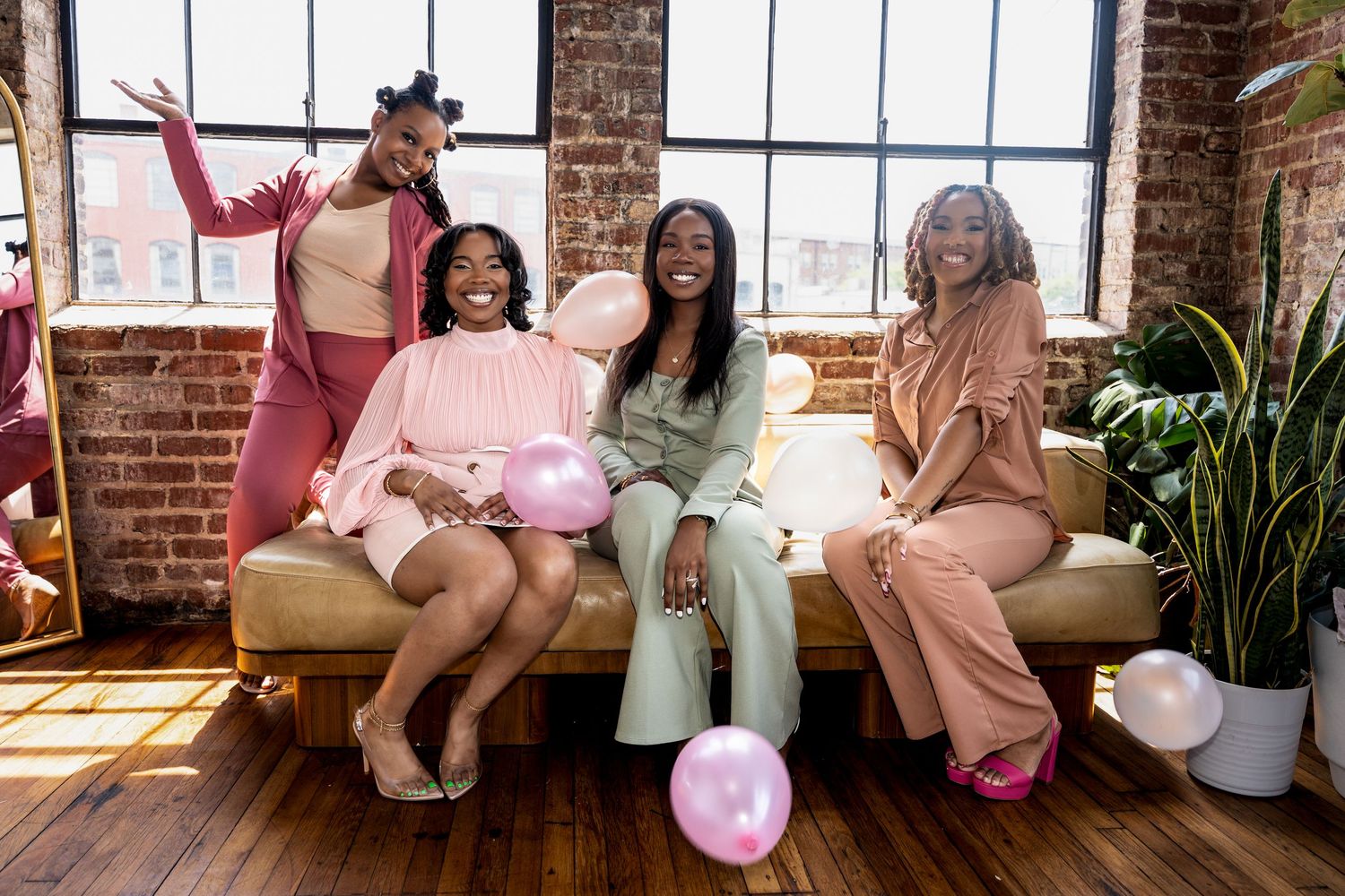 Friends celebrate together with balloons in a sunlit loft space with exposed brick walls and wooden floors.