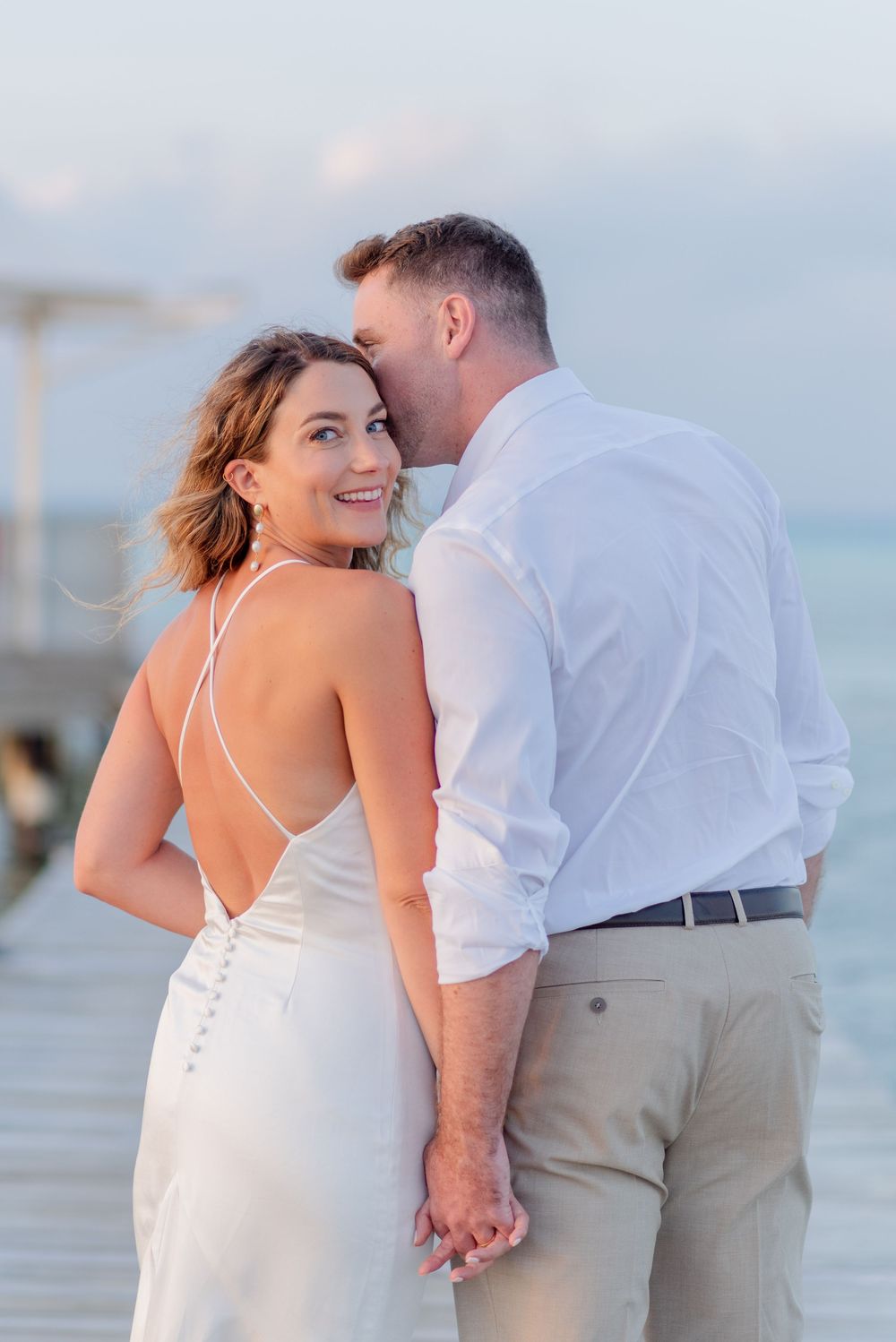 A romantic beach wedding couple shares tender moments at sunset in a white dress and khaki suit.