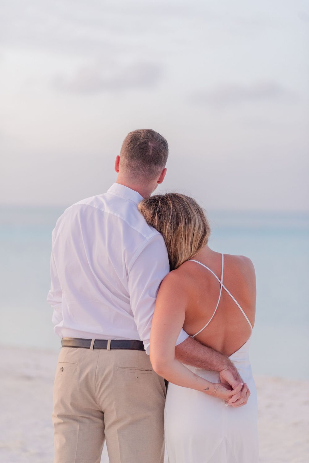 Couple walking together on a beach at sunset wearing white and beige clothing.