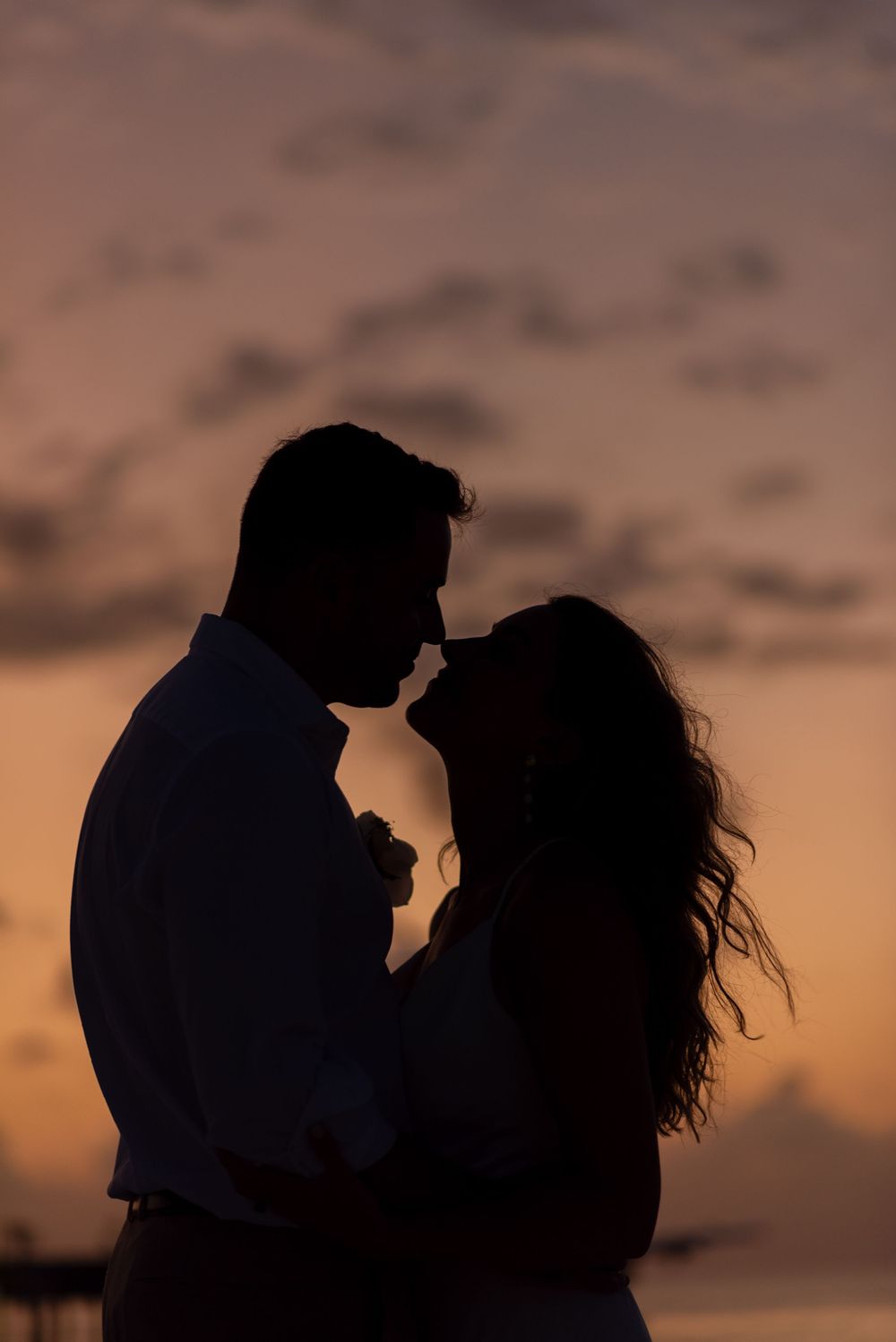 A romantic silhouette of a couple sharing an intimate moment against a warm sunset sky.